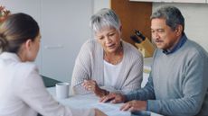 An older couple go over paperwork with a financial adviser at their kitchen table.