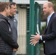 Prince William wearing a suit and talking to 2 men in black coats