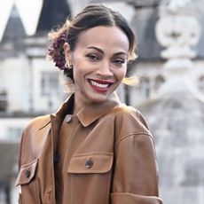 Zoe Saldana smiles wearing a brown jacket