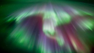 Vibrant green and purple aurora borealis streaking across the night sky, creating a mesmerizing celestial display with stars visible in the background.