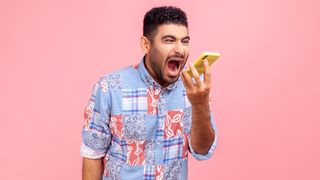 An angry-looking man holding up a smartphone and shouting at it.