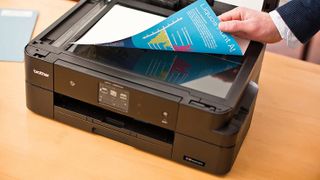 Best printers headline image showing someone pulling a freshly-printed color page off a Brother printer