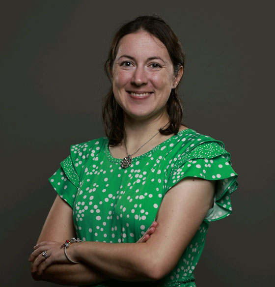 Woman in green shirt with crossed arms smiles for a headshot.