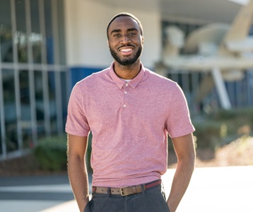 Young African American man stands outside smiling with hands in his pant pockets