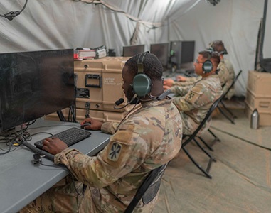 three US Serives members in tent working on computer network