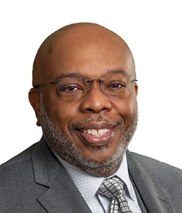 A man in a gray suit smiles at the camera