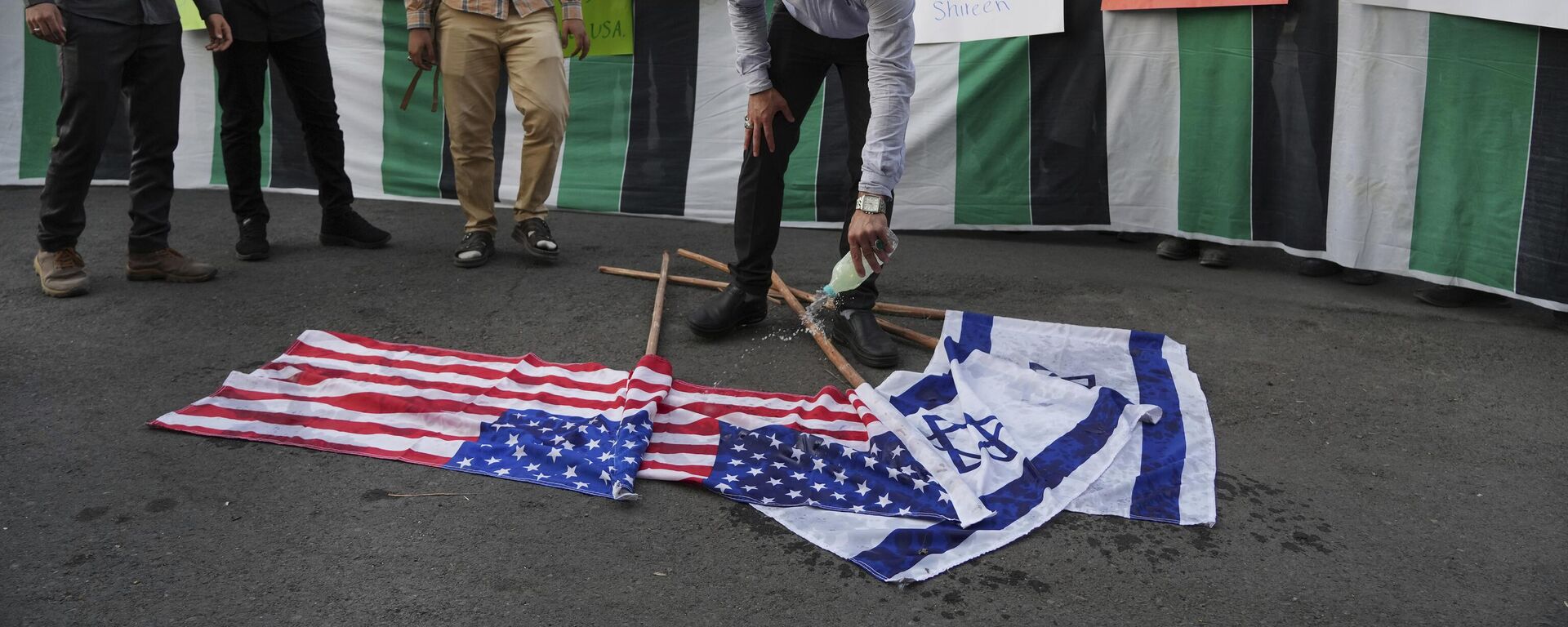 Manifestante derrama gasolina nas bandeiras de Israel e dos EUA antes de atear fogo a elas, durante um protesto em Teerã contra a viagem de Biden ao Oriente Médio. Irã, 16 de julho de 2022 - Sputnik Brasil, 1920, 11.12.2024