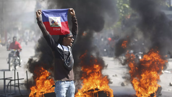 Manifestante segura bandeira do Haiti durante protesto que pede a saída do então primeiro-ministro, Ariel Henry, em meio à escalada da violência no país. Porto Príncipe, 2 de março de 2024 - Sputnik Brasil