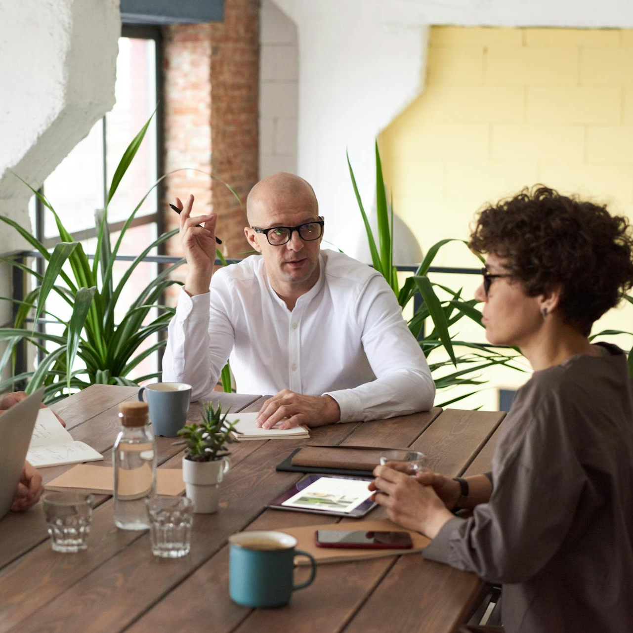 The picture shows 2 people sitting at a wooden table in what appears to be a meeting or a discussion - On the left, text reads: "Drive success - How Accessibility Enhances KPIs"