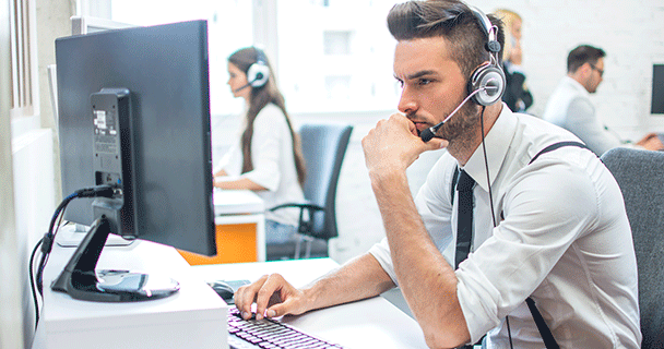 An image of a professional buyer wearing a headset carefully exams their computer screen in an open office space.