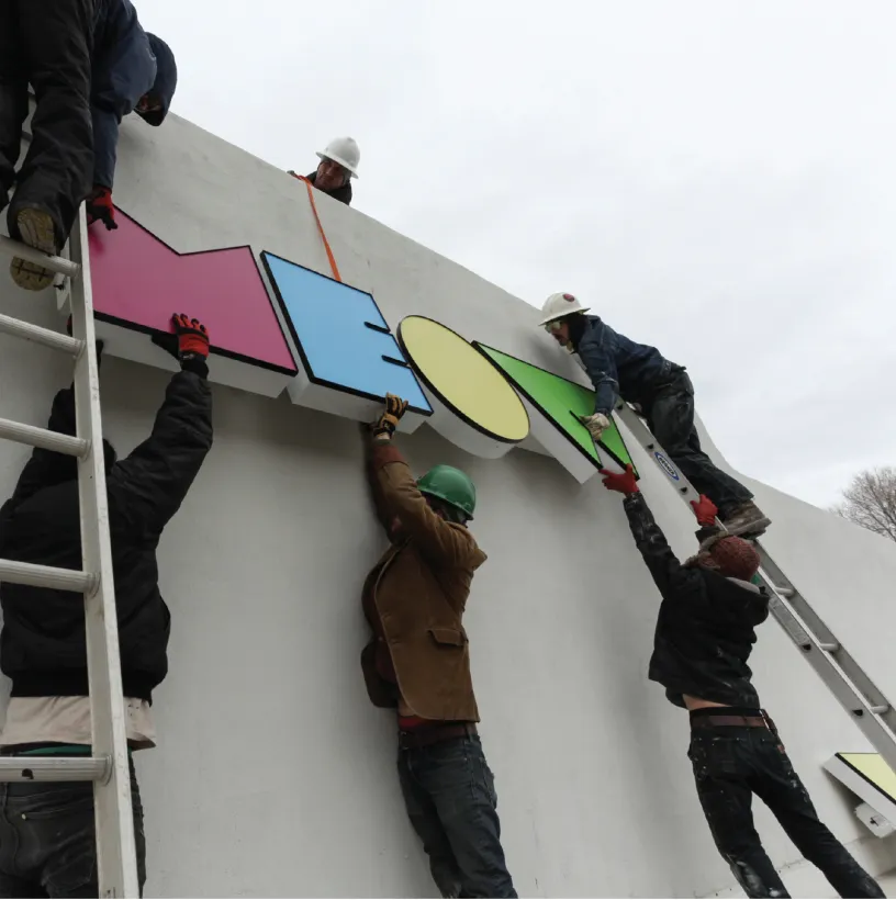 group of people hanging the Meow Wolf sign in Santa Fe on the building