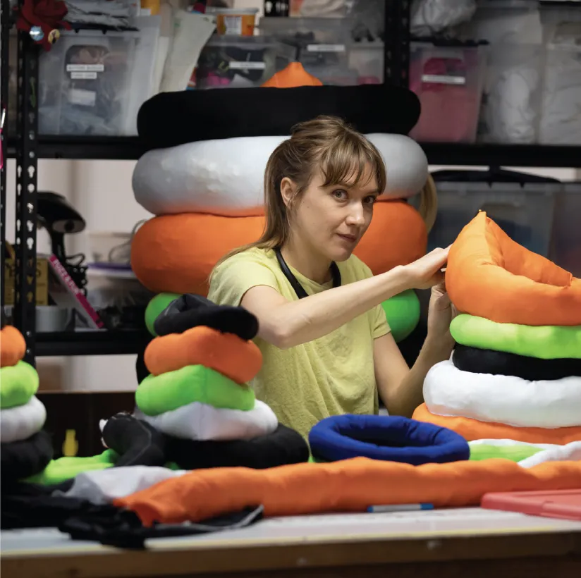 female-presenting person with brown hair stacking colorful circles of material to make giant worm shapes