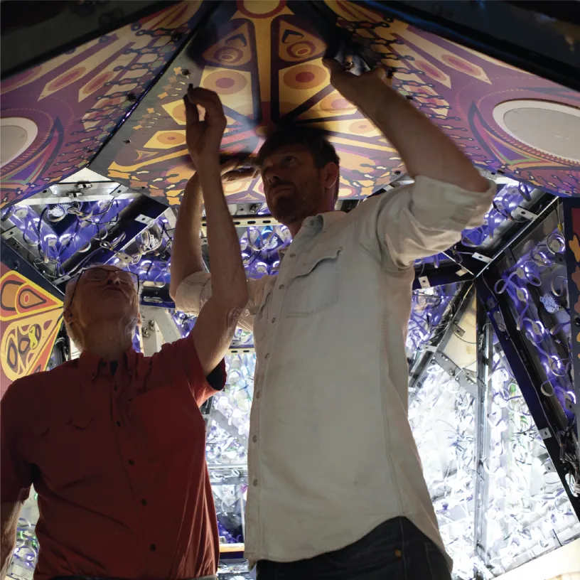 two people working on the ceiling of a piece of colorful, geometric art