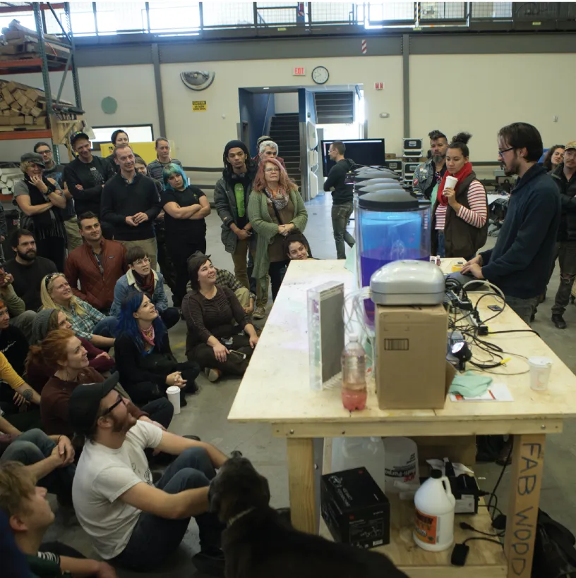 Large crowd of people sitting in front of a desk and a few people sitting behind the desk