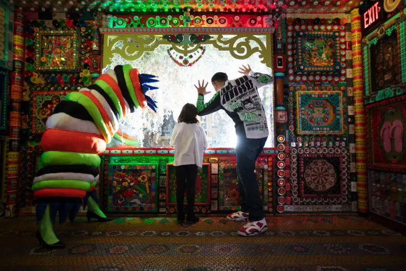 An adult, a child and a human sized worm look out a window in a colorful room. 