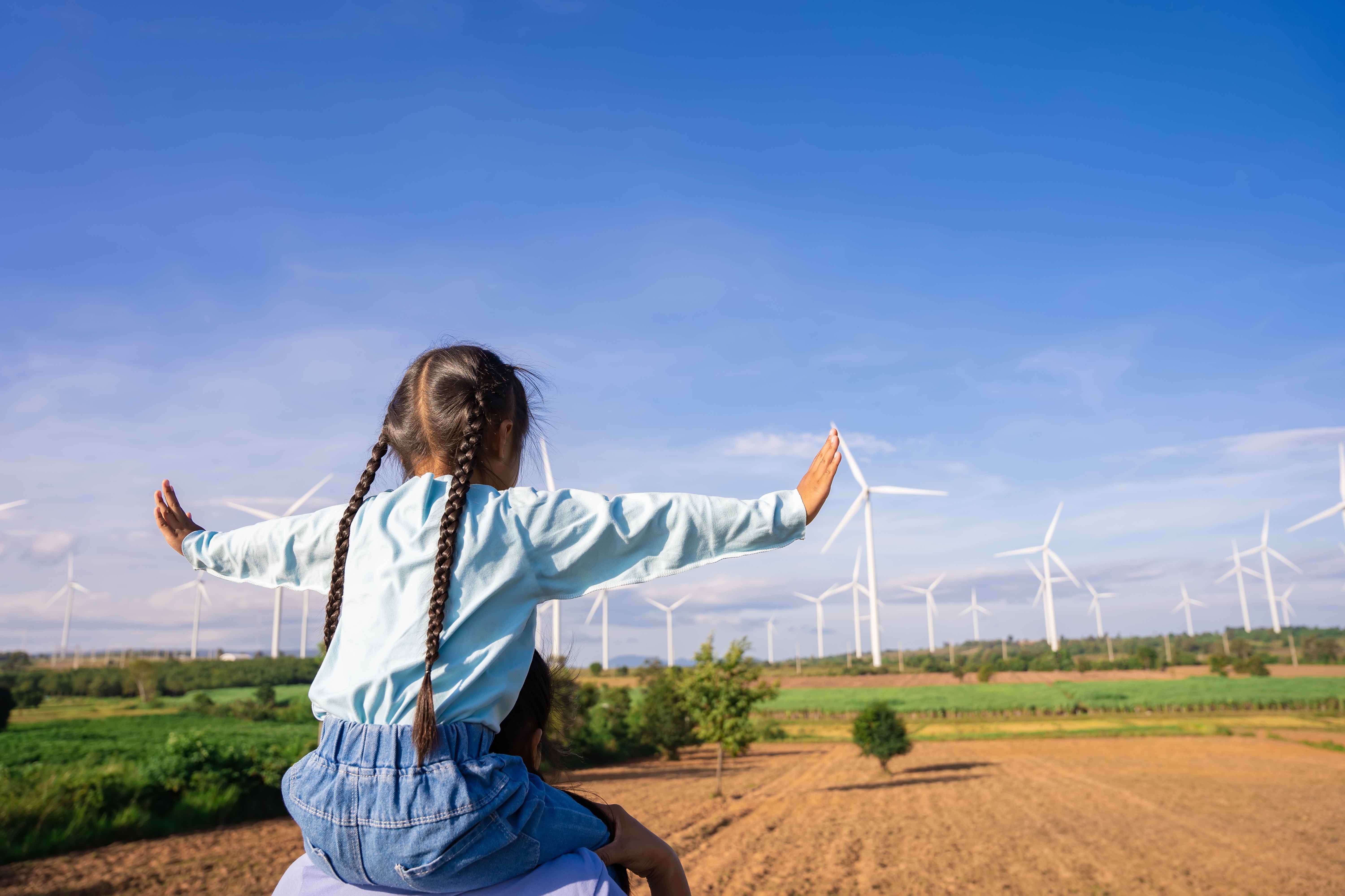 child and adult in front of a wind farm