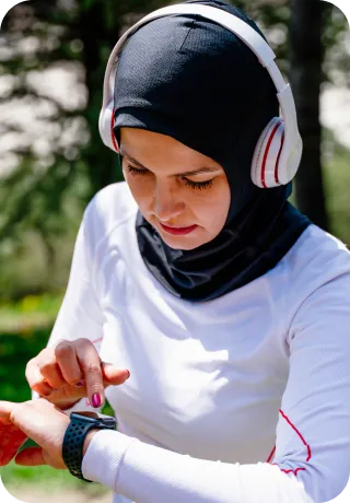 A woman in a headscarf and headphones looks at her watch