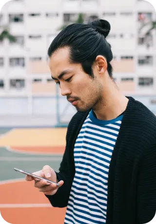 A man sitting on a bench, focused on his phone, typing a text message