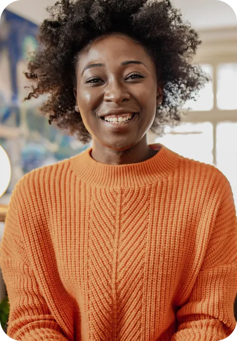 A cheerful woman in an orange sweater smiling warmly at the camera.