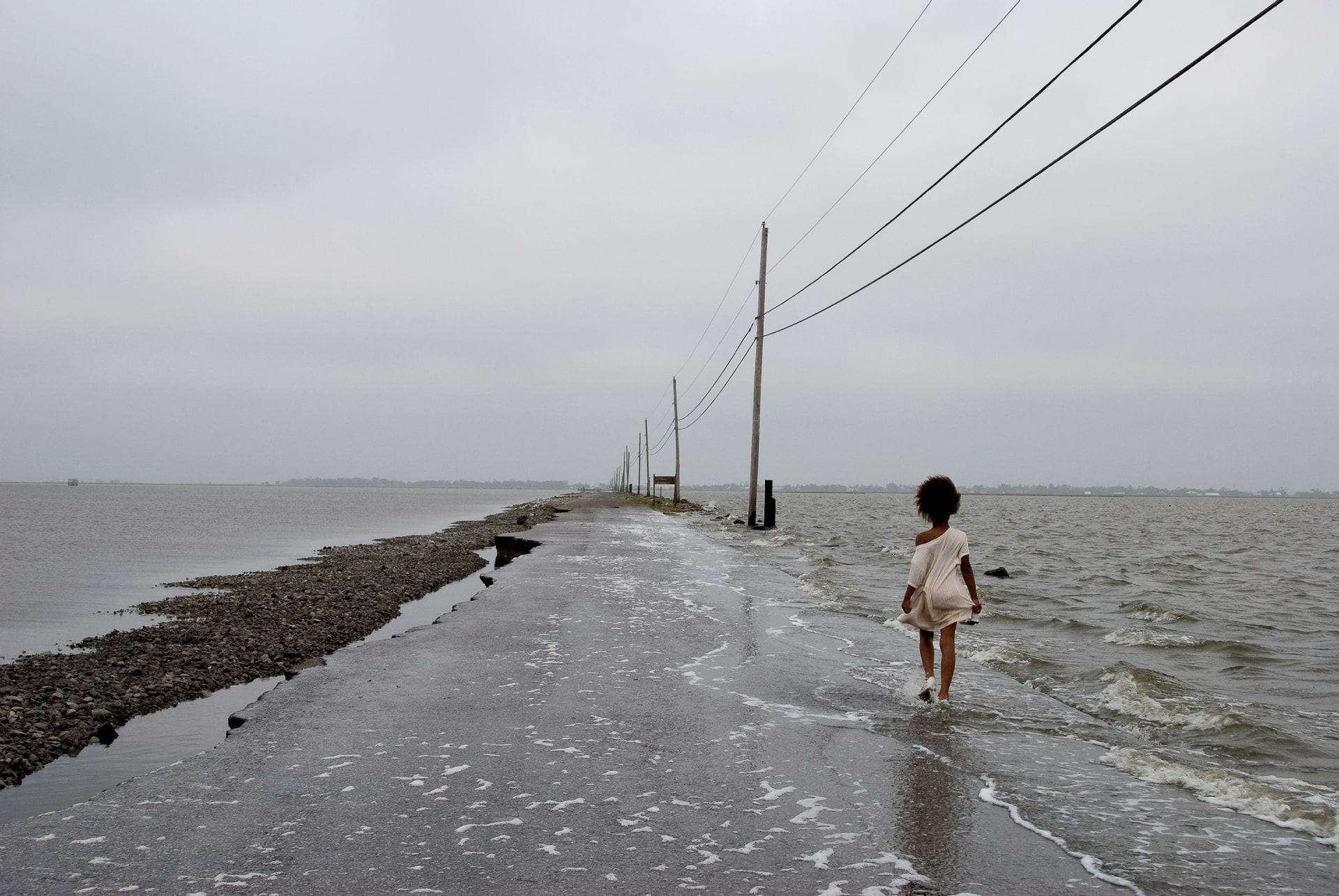 A young girl walks along a ruined, flooded road in Isle de Jean, Louisiana.
