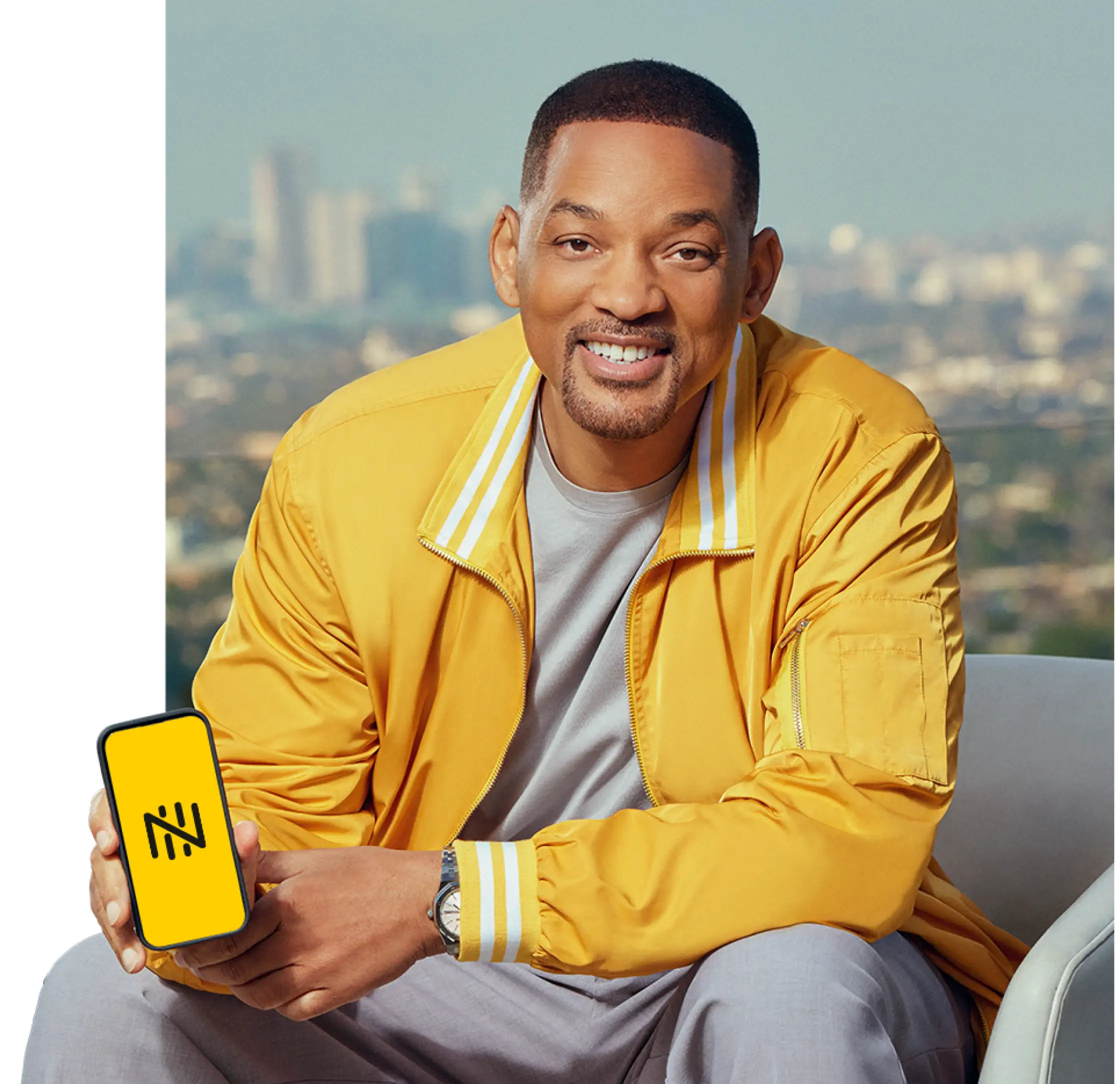 Will smith com casaco amarelo sorrindo com o celular mostrando o logo da Fintech Nomad