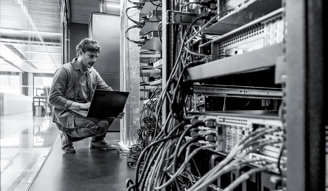 Black & white photo of a cybersecurity technician analyzing server stacks. 