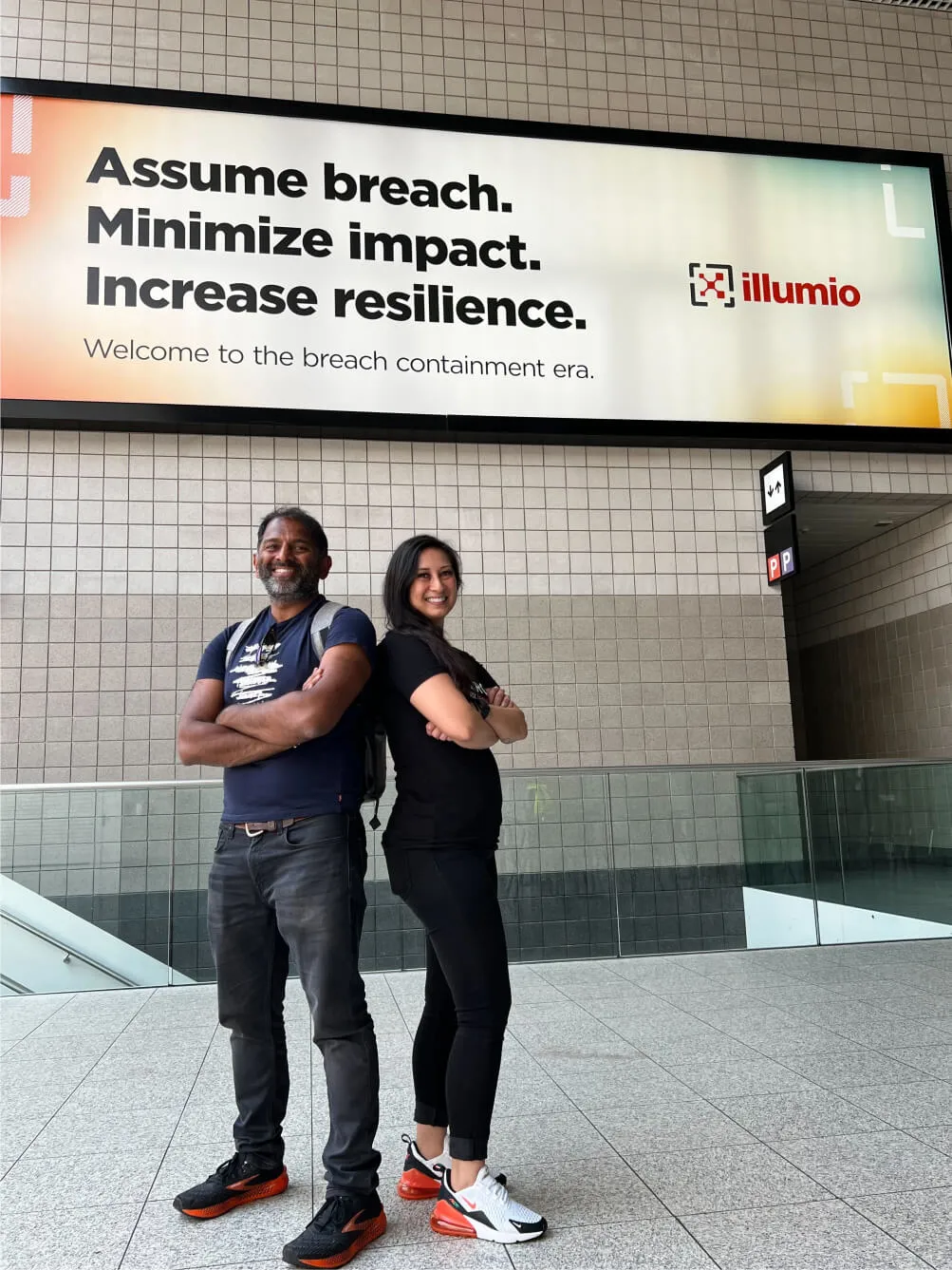 Two Illumio reps standing in front of a sign saying 'Assume breach. Minimize impact. Increase resilience. Welcome to the breach containment era.'