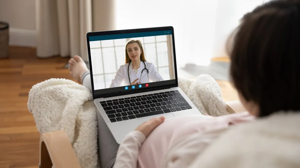 Pregnant woman at home doing a video consultation with a doctor on her laptop