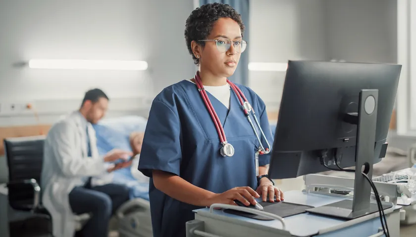 Medical professional standing and looking at a computer monitor in a hospital