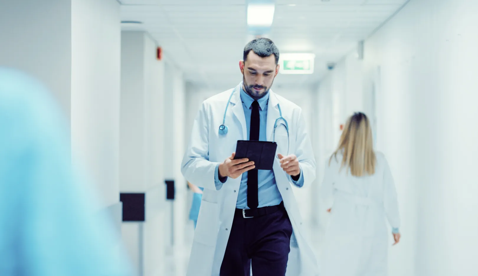 Medical professional walking in a hospital corridor while looking at a digital tablet