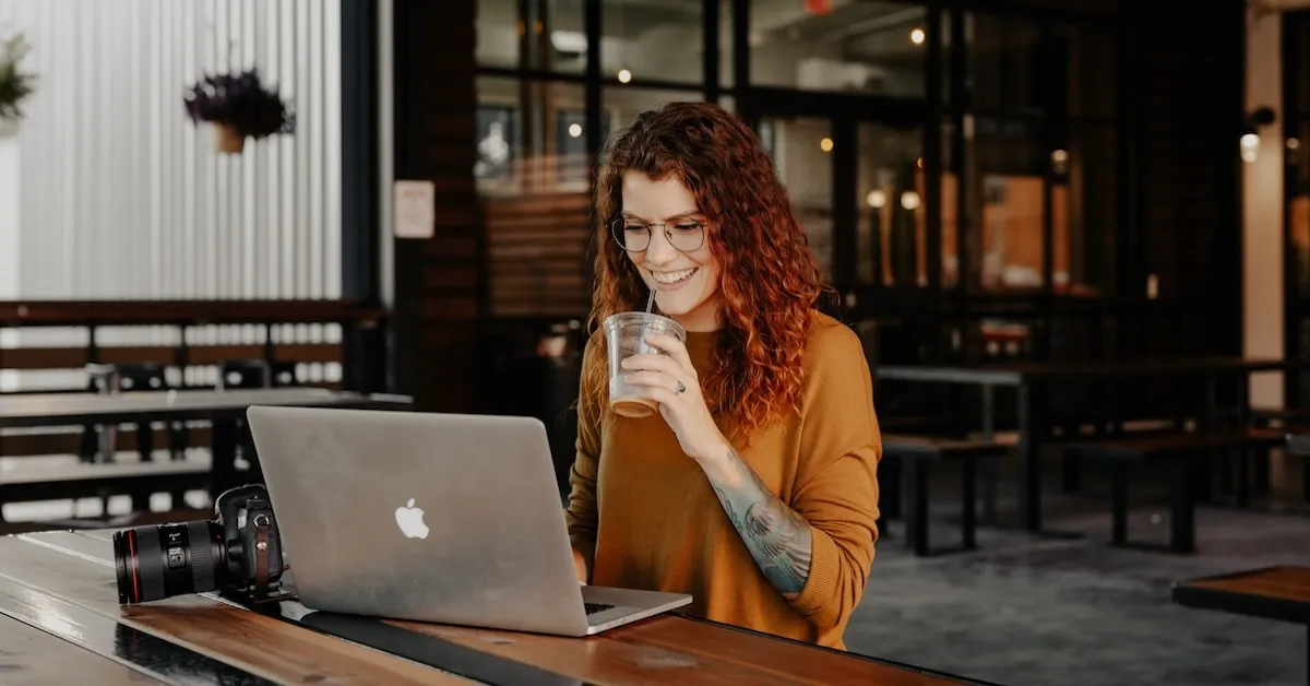 Woman works on a laptop and drinks a coffee outside a coffee shop. 