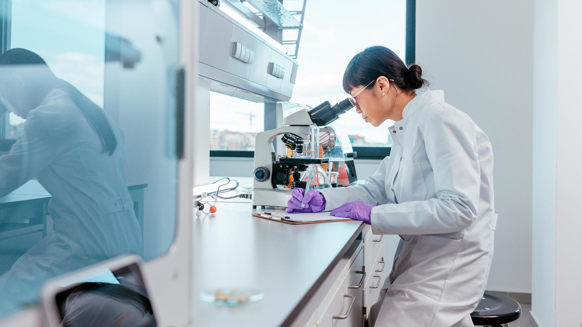 Female scientist looking trough the microscope writing down her discoveries 