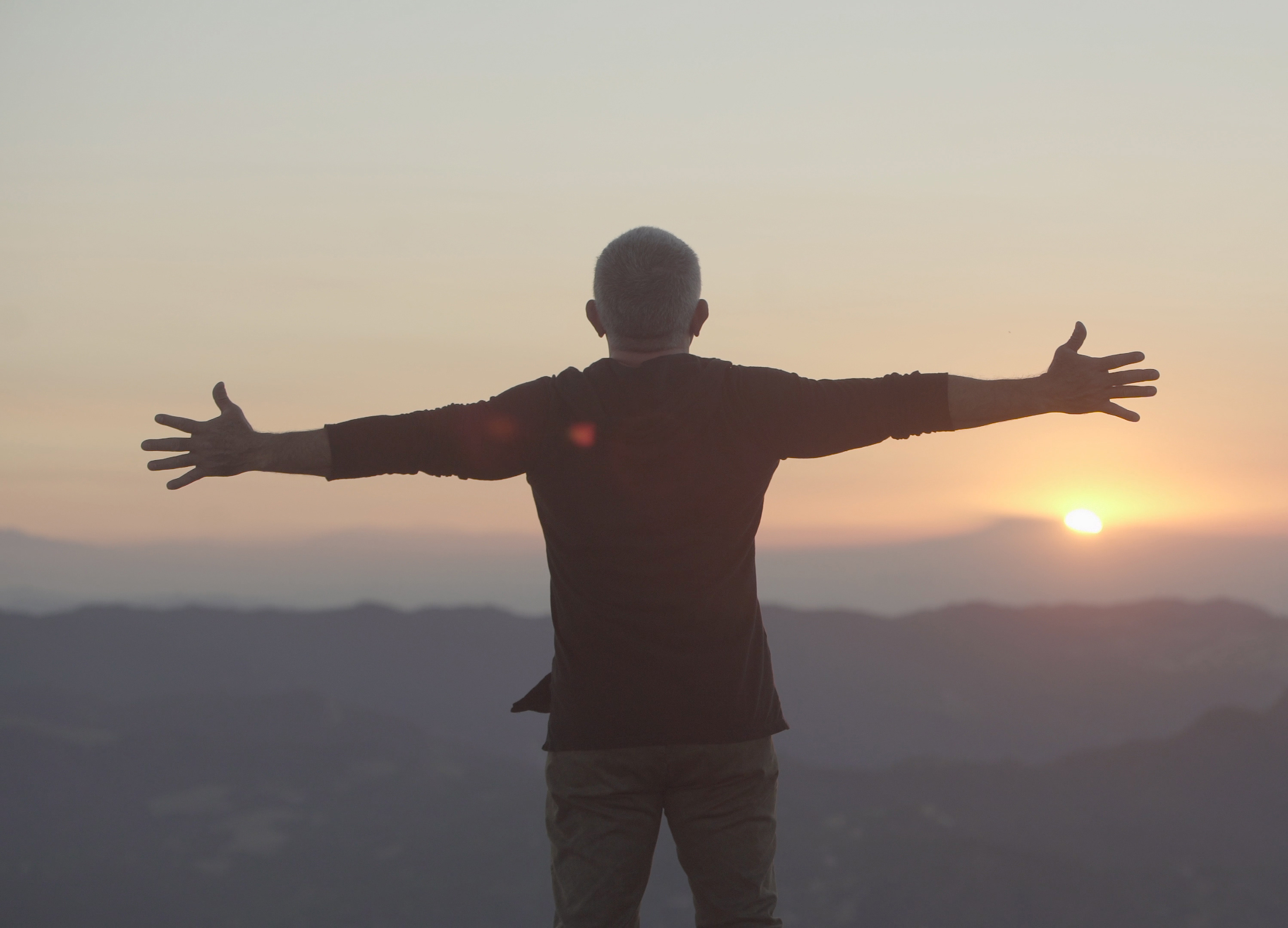 Cesar Millan with arms open watching a sunset