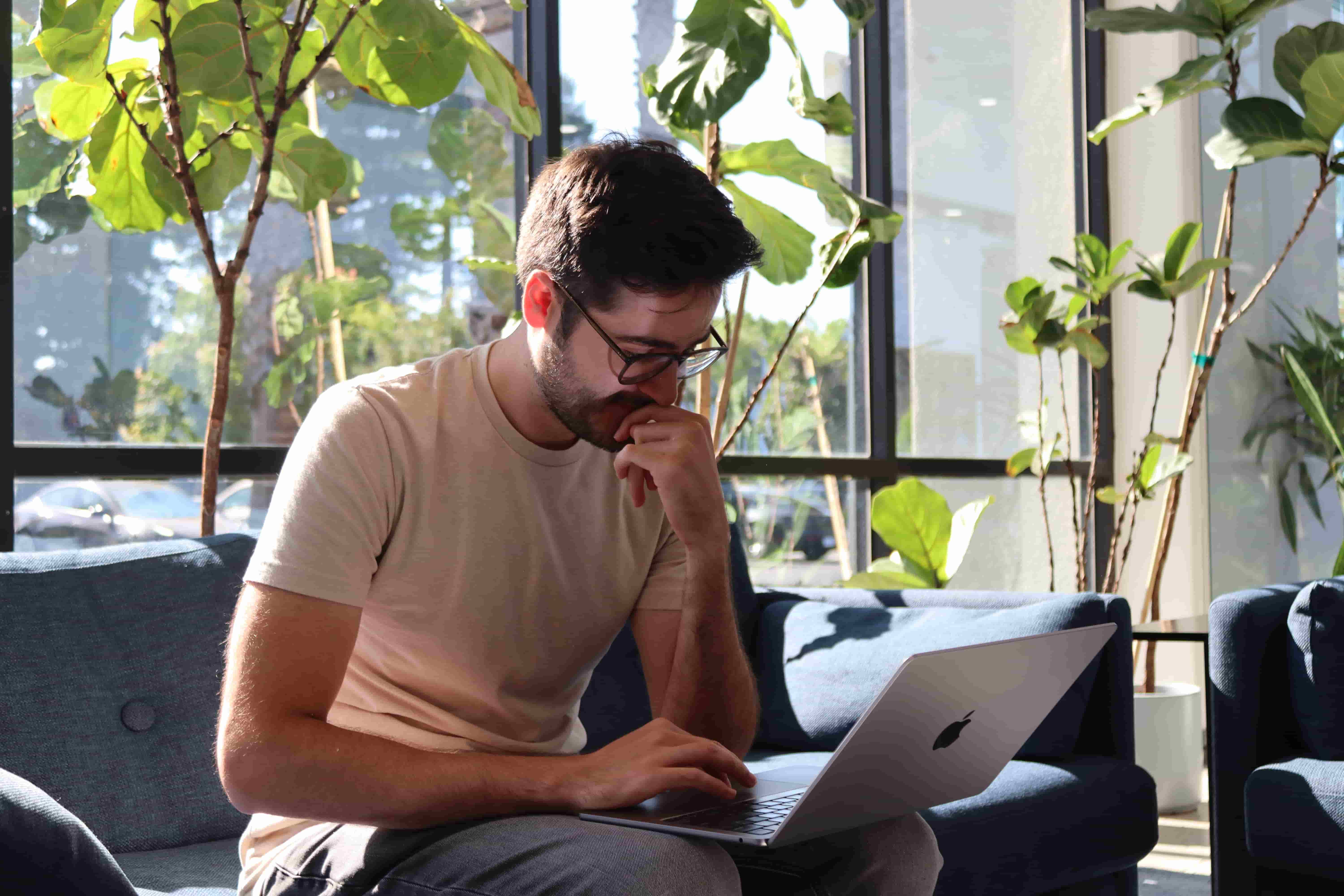 Richie Goulazian seated on a couch and working on a laptop that rests on his knees.