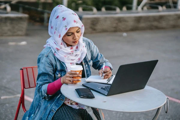 A small business owner runs online payroll from her laptop at an outdoor café.