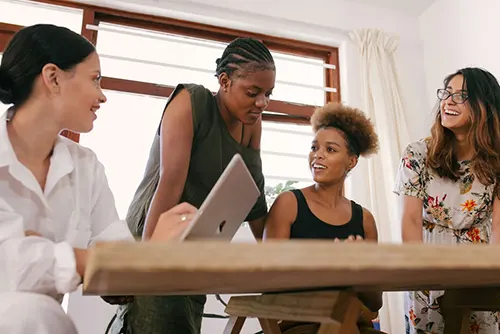 Four employees gather around desk with laptop to discuss small business benefits.