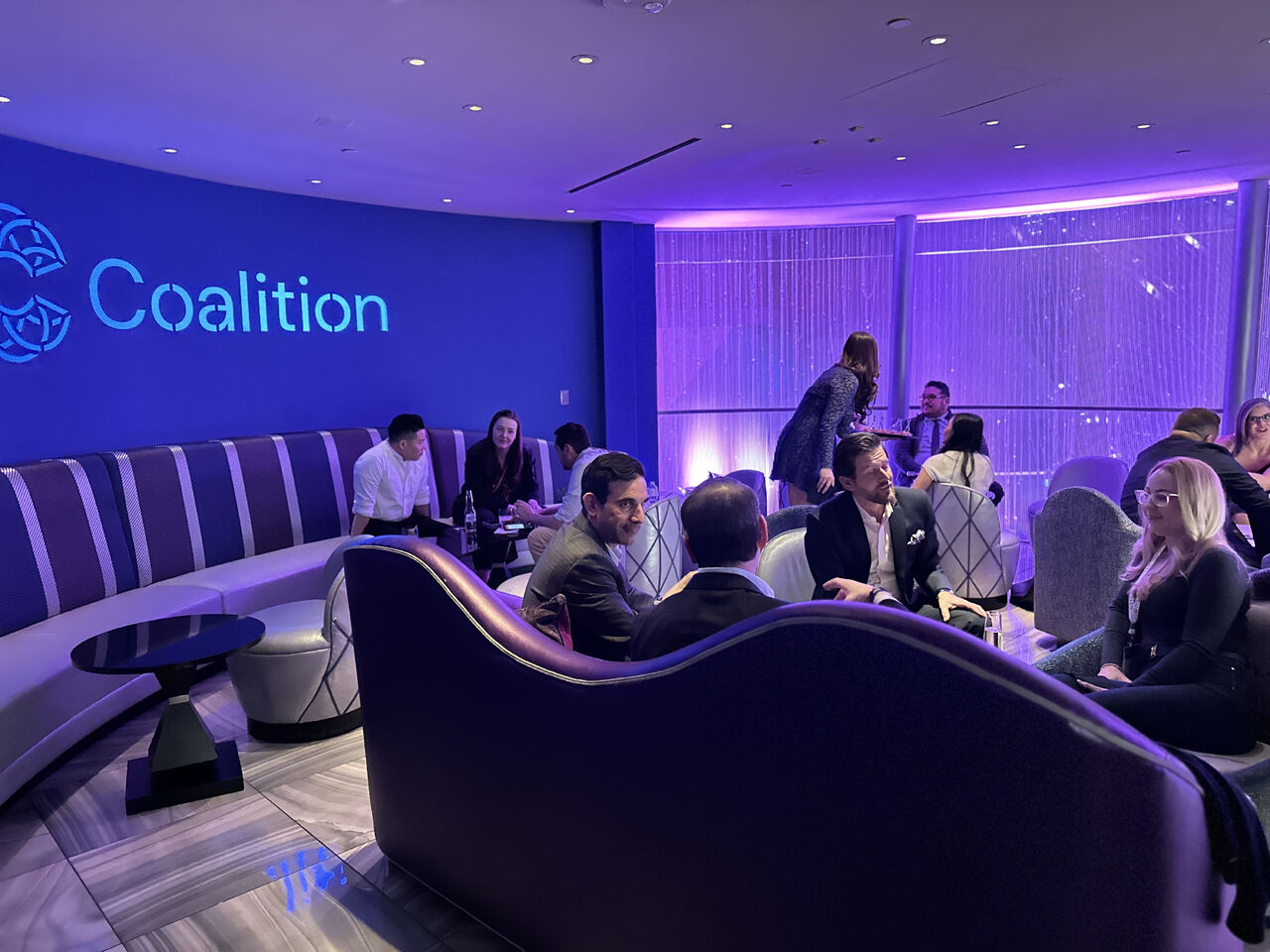 Coalition employees gathering on a sofa in front of a Coalition backdrop.