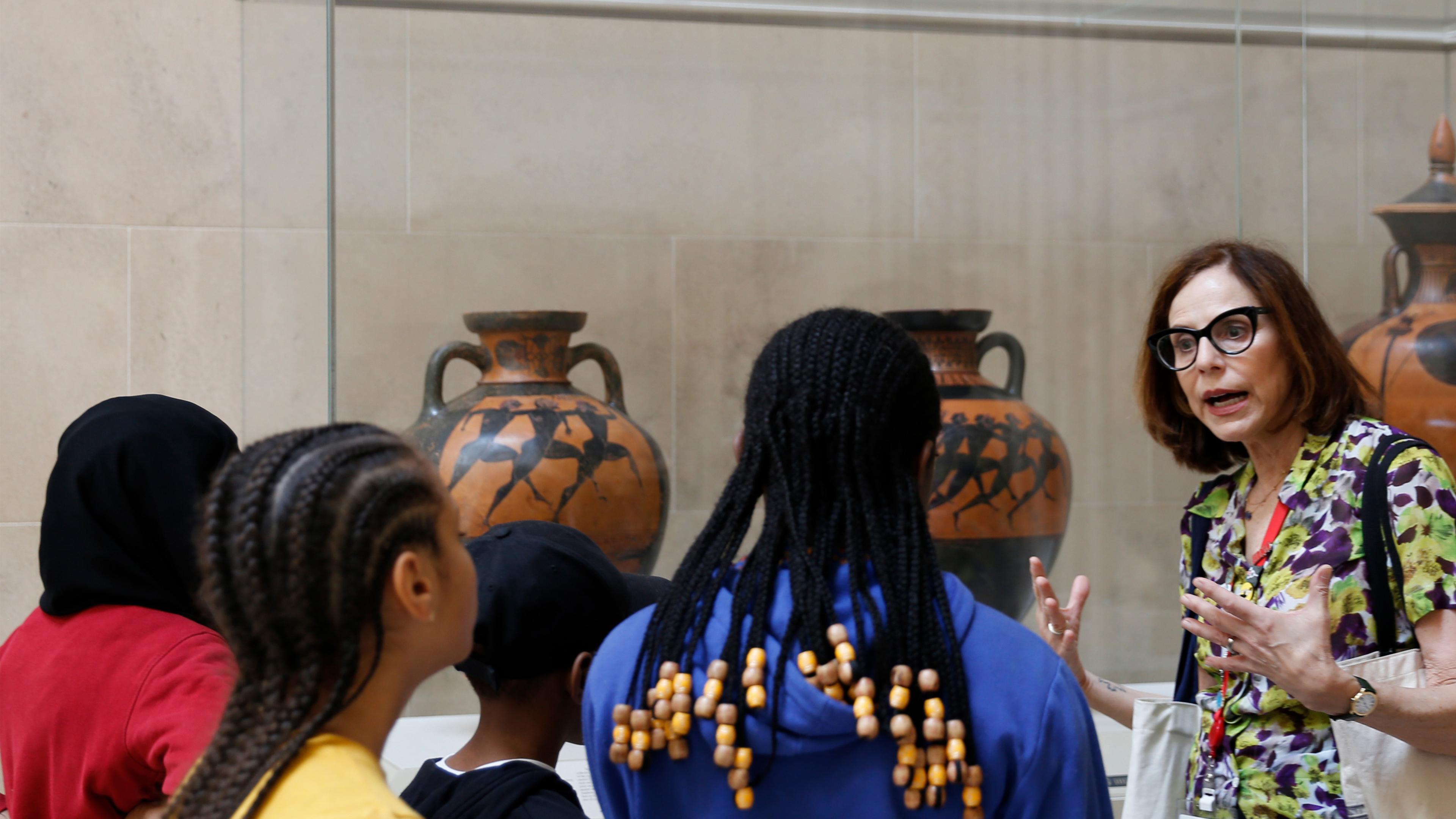 A group of young kids being led through the Greek and Roman Galleries by a docent.