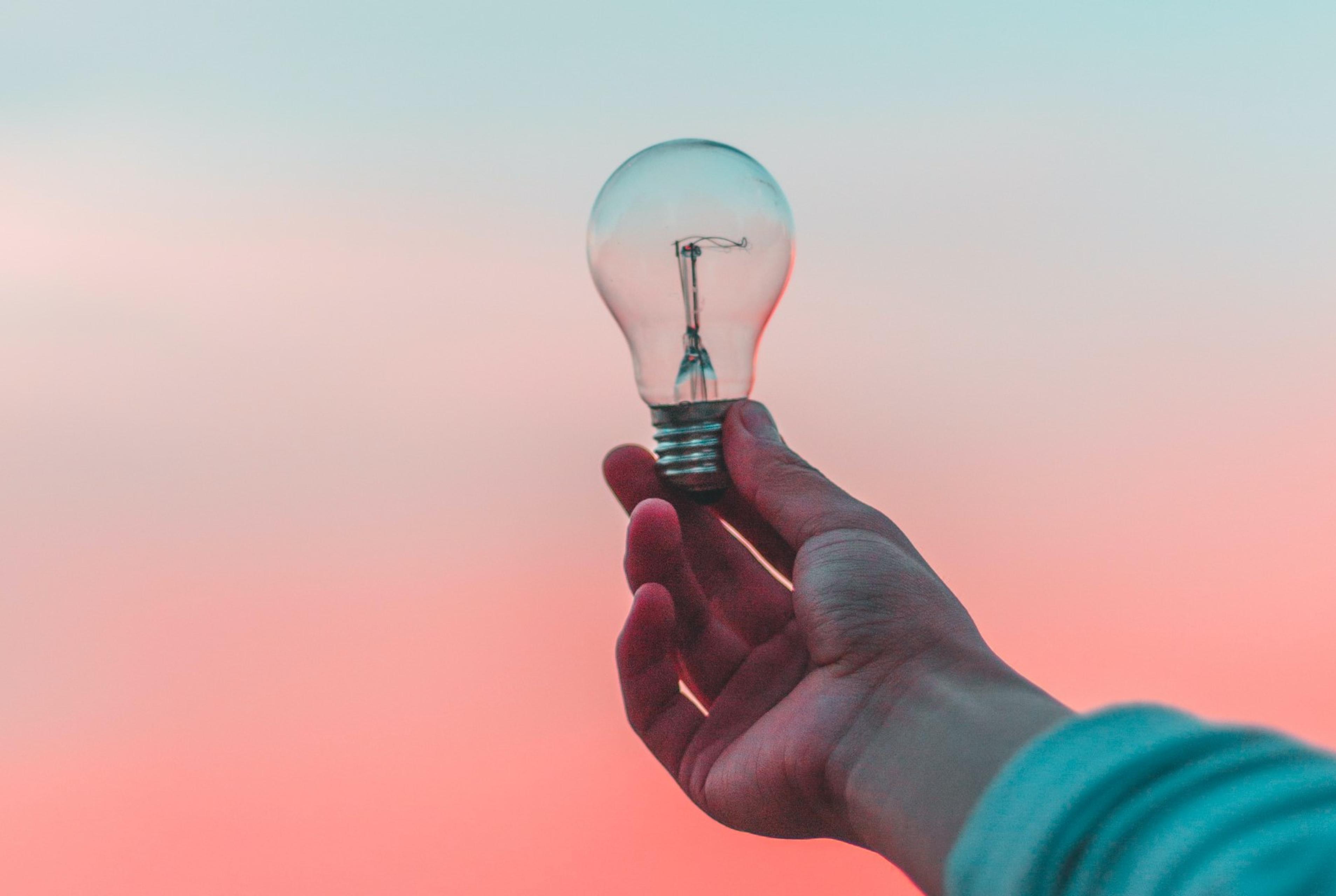 Hand holding a lightbulb up against pink skies