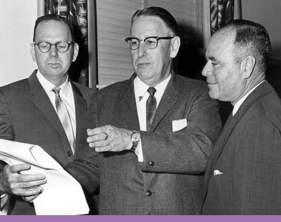 Three men look at a paper