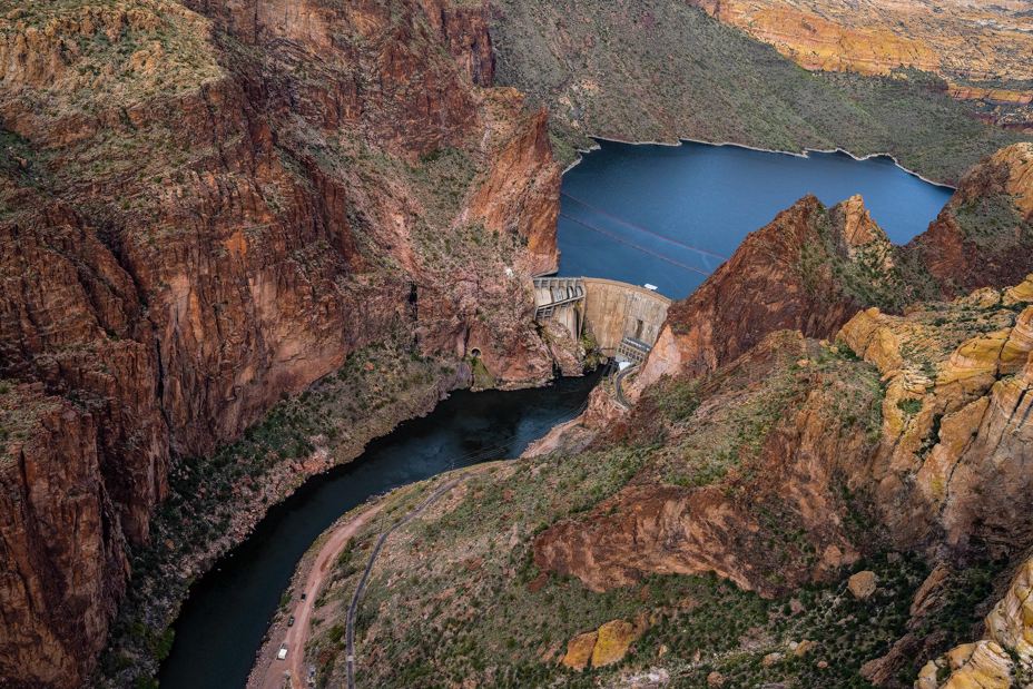 aerial photo of dam across rocky canyon with reservoir behind and river curving away