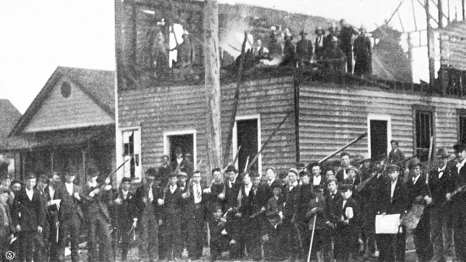 Men gather outside the charred remains of The Daily Record after the 1898 massacre.