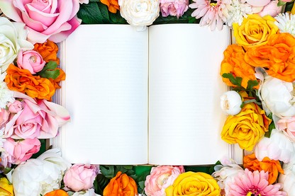 An open blank book surrounded by roses and other flowers