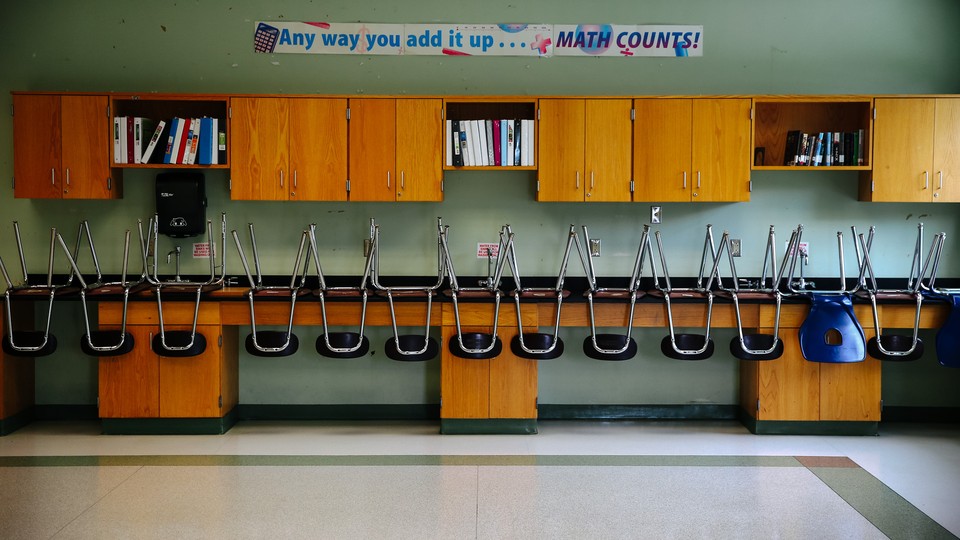 An empty classroom with a row of empty, upside-down chairs on a long desk