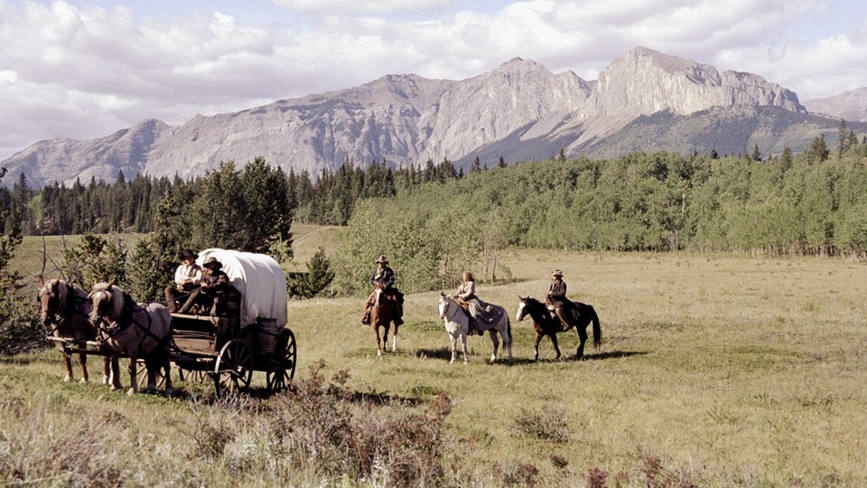people ride in a covered wagon with mountains in the background