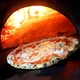 A pizza in front of an open brick oven