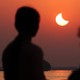 The silhouette of two people watching a partial solar eclipse in a deep-orange sky