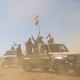 Houthi fighters and tribesmen rally with flags in the back of a pickup truck surrounded by desert dust.