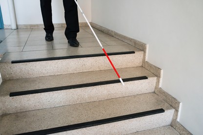 A man walks down a flight of stairs with the help of a white cane.