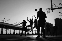 Black-and-white photo of silhouetted people playing basketball on an outdoor court